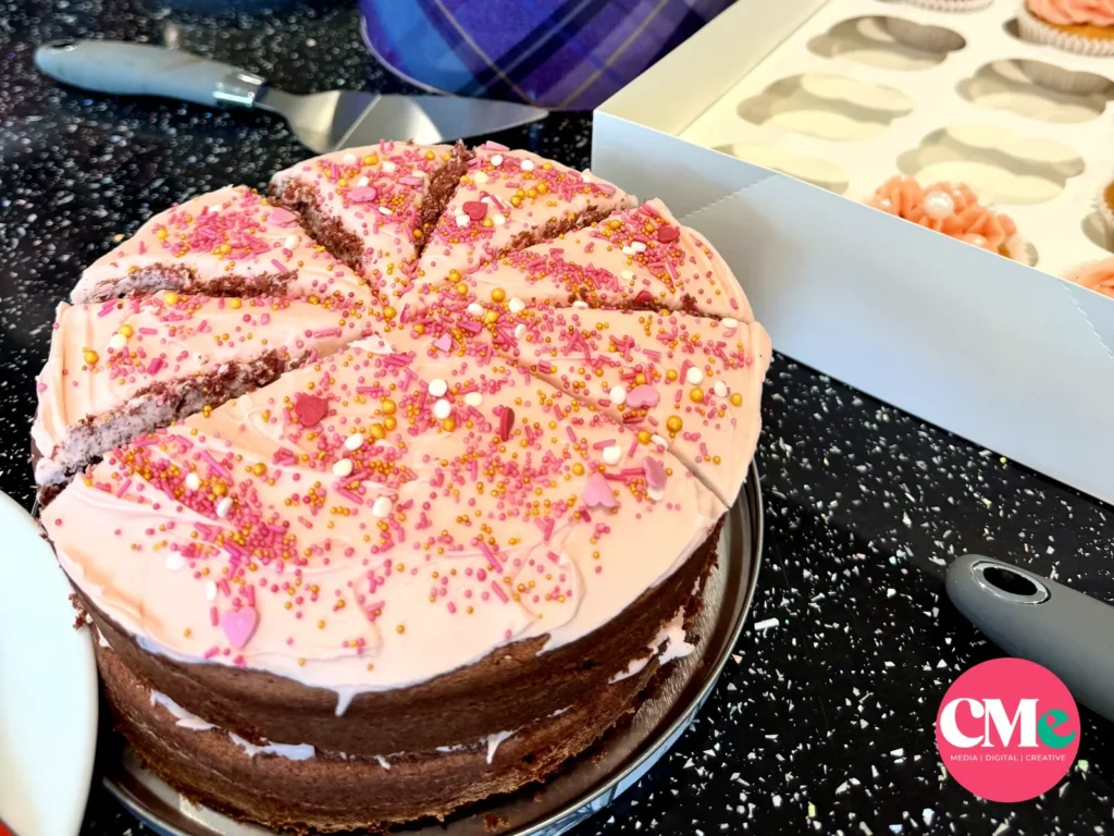 A pink iced layer cake with sprinkles, cupcakes and brownies at the CMe Media bake sale