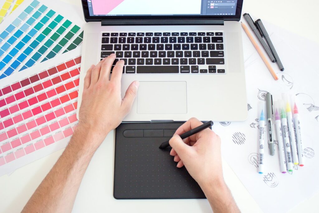 Graphic designer creating display ad artwork with a drawing tablet, laptop and colour swatches