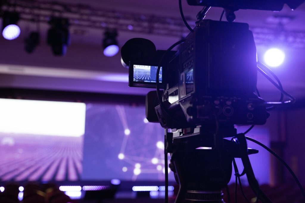 Broadcast video camera on a tripod filming a stage