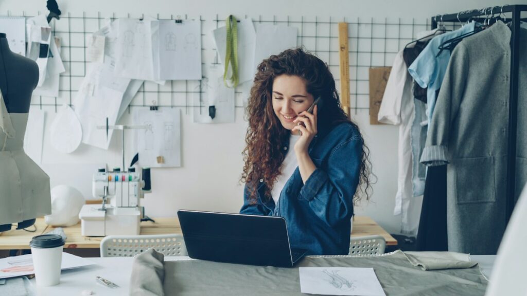 Small business owner working on a laptop in her shop while on the phone