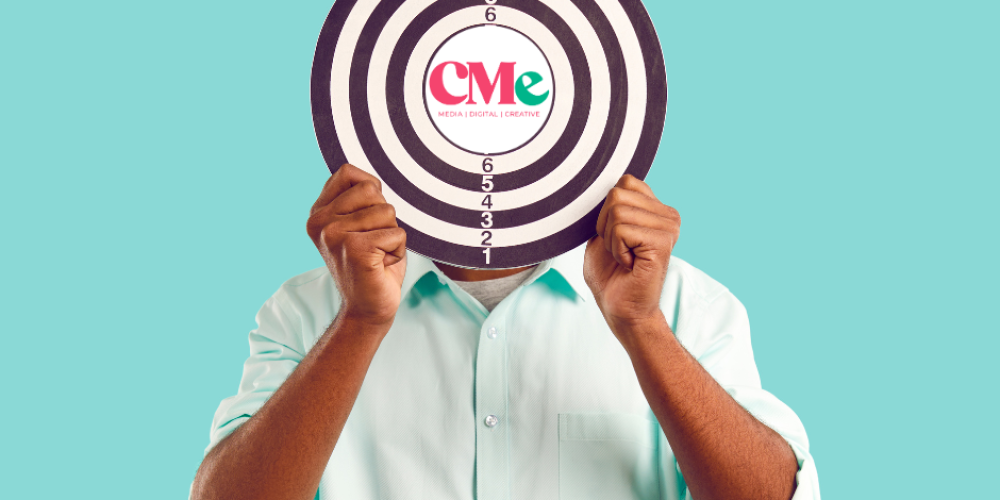 A person holding up a black and white target board, with the CMe Media logo in the centre, against a light teal background