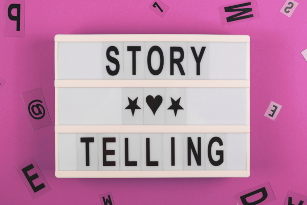A 3 lined, white light box with the words, story on the first line, telling on the 3rd line. A heart image is on the second line. with a pink background