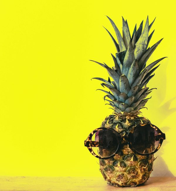 A pineapple wearing a pair of sunglasses against a yellow background