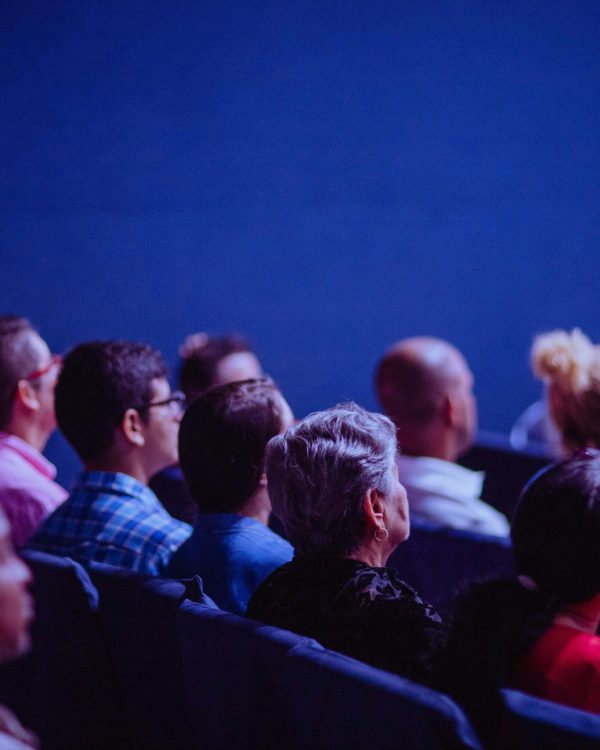 people sitting in rows of seat looking forward, whilst being pictured from the back right hand side.