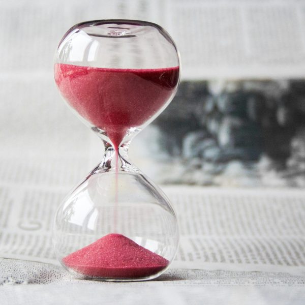 A glass egg timer, with pink sand flowing through it