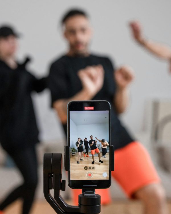 3 people dancing in front of a mobile phone. The phone is at the front of the picture and the people are blurred