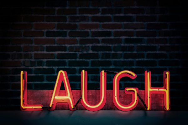 A red, neon sign saying laugh, against a dark, brick background